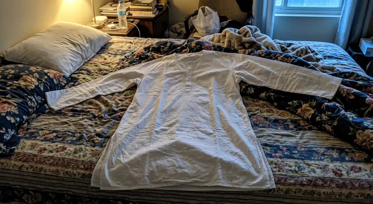 Amateur DIY marketplace listing photo of white kurta — uneven lighting, wrinkled fabric, phone camera quality before ShotRoom AI photoshoot